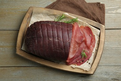 Photo of Tasty bresaola, peppercorns and rosemary on wooden table, top view