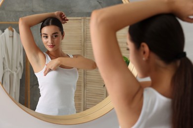 Photo of Beautiful young woman doing breast self-examination near mirror in bathroom