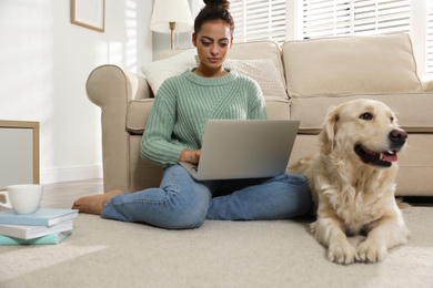 Photo of Young woman with laptop and her Golden Retriever at home. Adorable pet