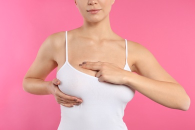 Woman checking her breast on color background, closeup