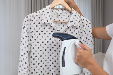 Photo of Woman steaming blouse on hanger at home, closeup