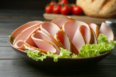 Photo of Slices of delicious boiled sausage with lettuce on dark wooden table, closeup