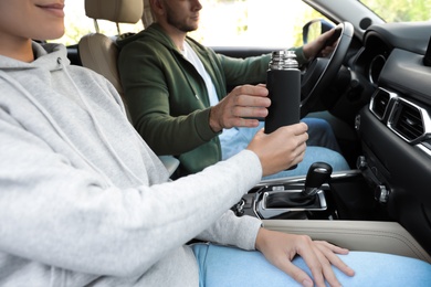 Woman with thermos on passenger seat of car, closeup
