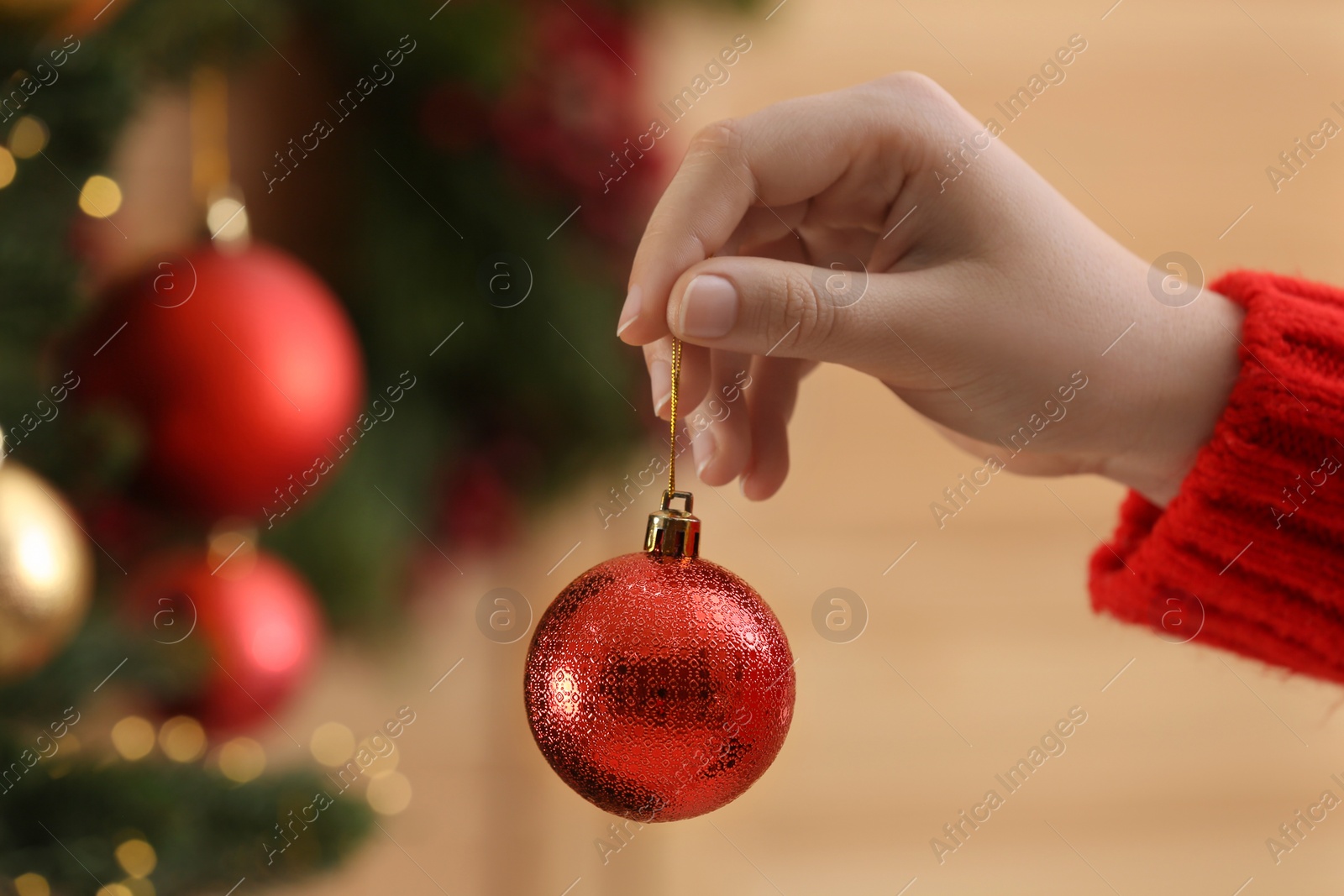 Photo of Woman holding red ball near Christmas tree indoors, closeup