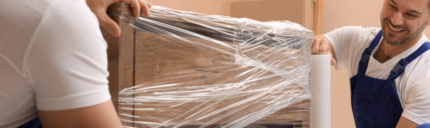 Image of Workers wrapping chest of drawers in stretch film indoors. Banner design