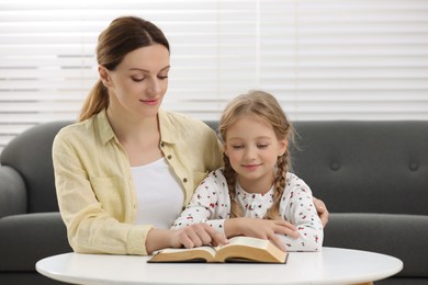 Photo of Girl and her godparent reading Bible together at table indoors