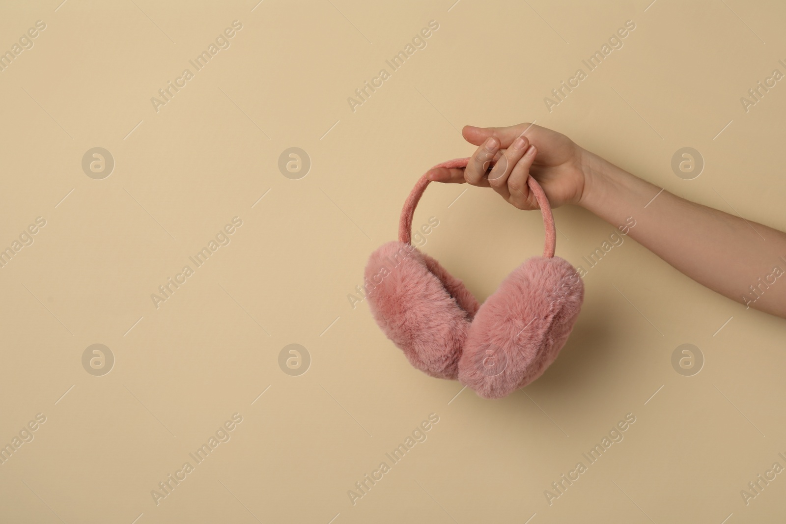 Photo of Woman holding stylish winter earmuffs on beige background, closeup. Space for text