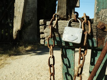 Photo of Old wooden fence with metal chain and lock on sunny day, space for text