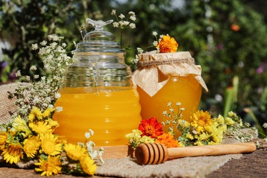 Delicious fresh honey and beautiful flowers on wooden table in garden