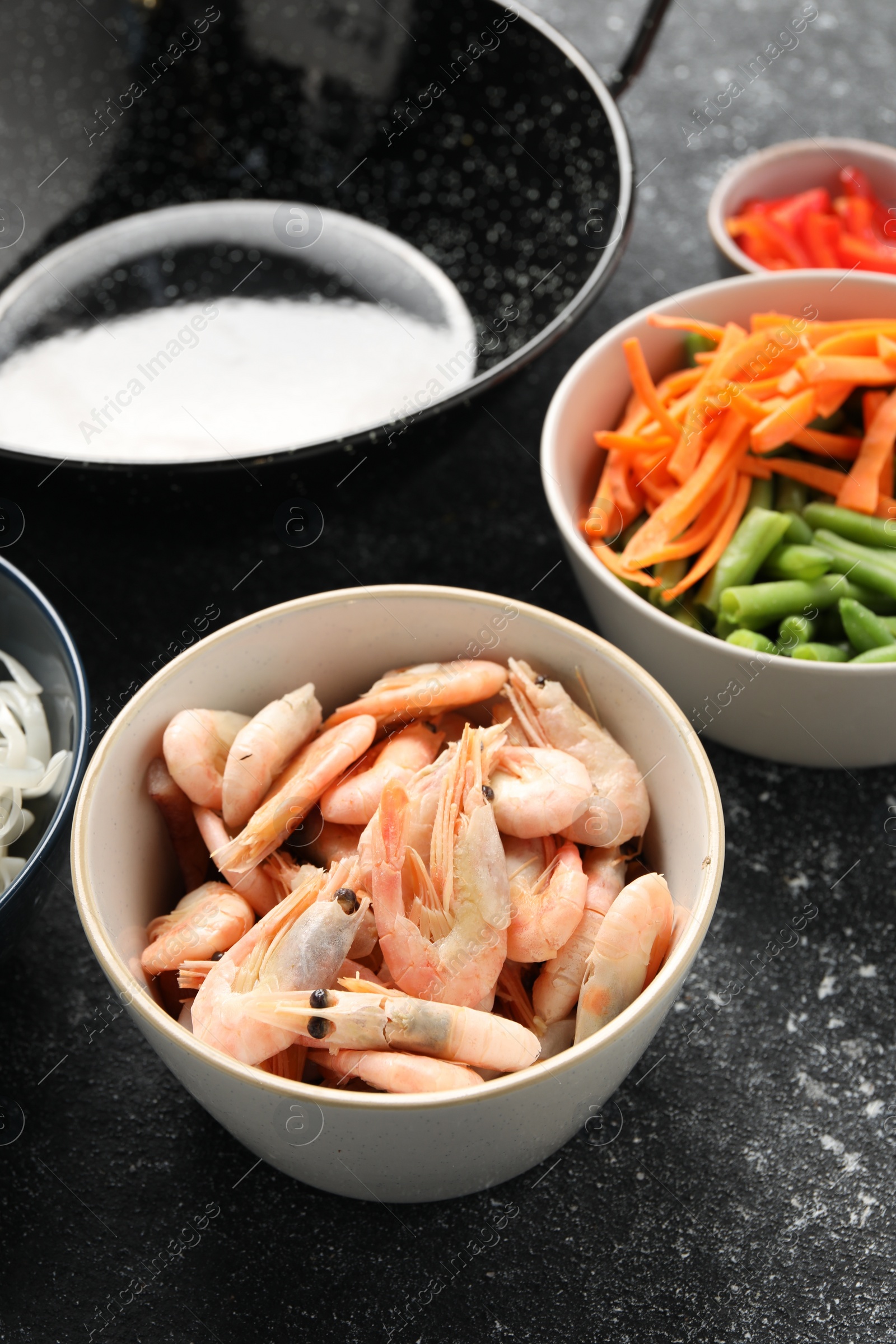 Photo of Shrimps, vegetables and black wok on grey textured table, closeup