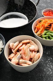 Shrimps, vegetables and black wok on grey textured table, closeup