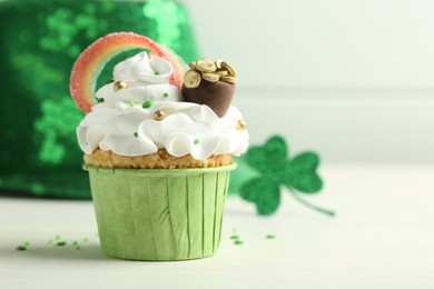 St. Patrick's day party. Tasty cupcake with sour rainbow belt and pot of gold toppers on white table, closeup. Space for text