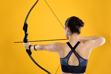 Photo of Woman with bow and arrow practicing archery on yellow background, back view