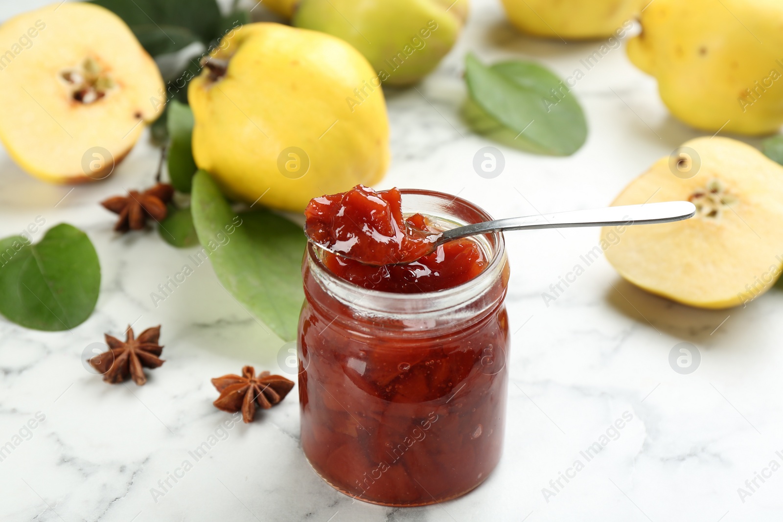Photo of Delicious quince jam and anise stars on white marble table, closeup