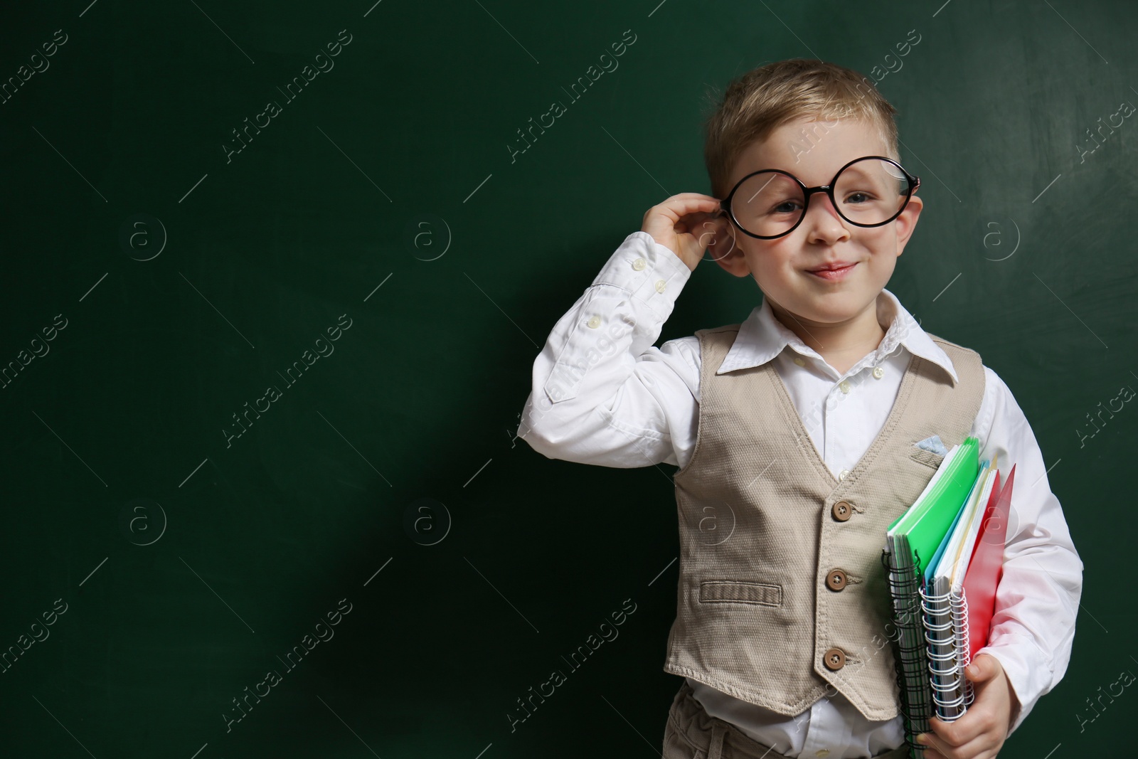 Photo of Cute little child wearing glasses near chalkboard, space for text. First time at school