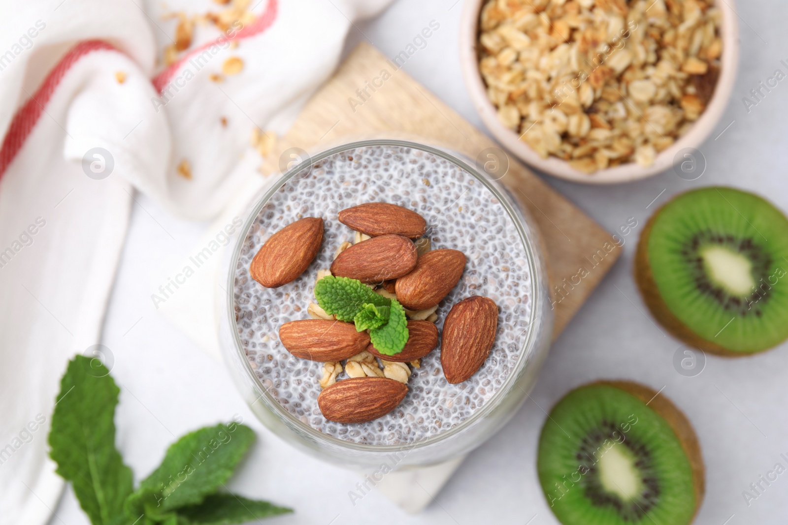 Photo of Delicious dessert with chia seeds, almonds and fresh cut kiwi fruits on light table, flat lay