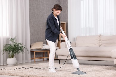 Happy young housewife vacuuming carpet at home