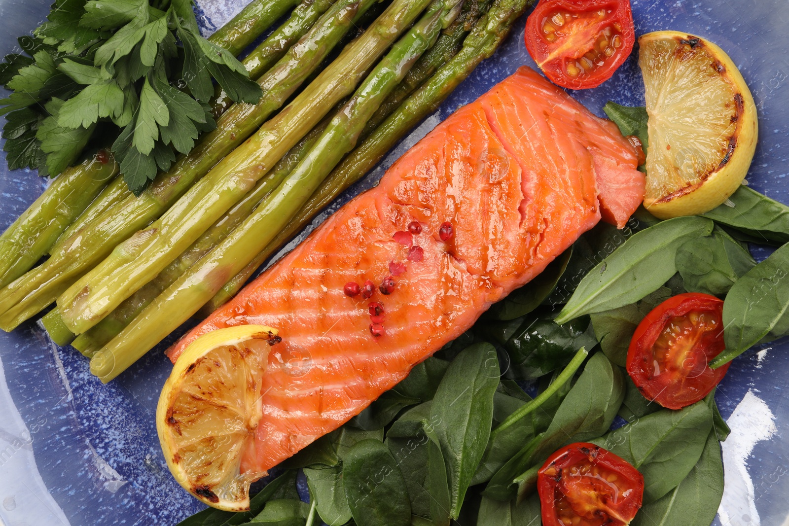 Photo of Tasty grilled salmon with tomatoes, asparagus, lemon and basil on plate, top view