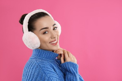 Beautiful young woman wearing earmuffs on pink background. Space for text