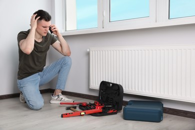 Photo of Handyman with pipe wrench talking on phone near radiator in room