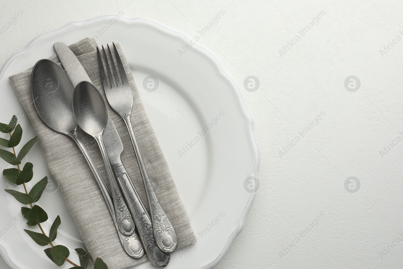 Photo of Stylish setting with cutlery, eucalyptus leaves and plate on white textured table, top view. Space for text