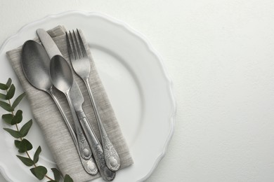 Photo of Stylish setting with cutlery, eucalyptus leaves and plate on white textured table, top view. Space for text