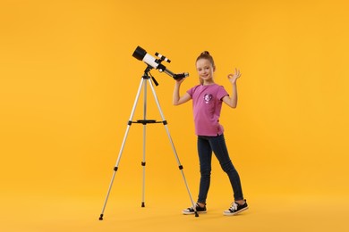 Photo of Happy little girl with telescope showing ok gesture on orange background