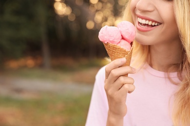 Photo of Happy young woman with delicious ice cream in waffle cone outdoors, closeup. Space for text