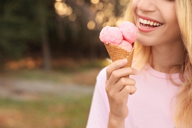 Happy young woman with delicious ice cream in waffle cone outdoors, closeup. Space for text