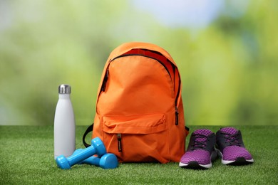 Photo of Backpack and different sports equipment on grass against blurred background