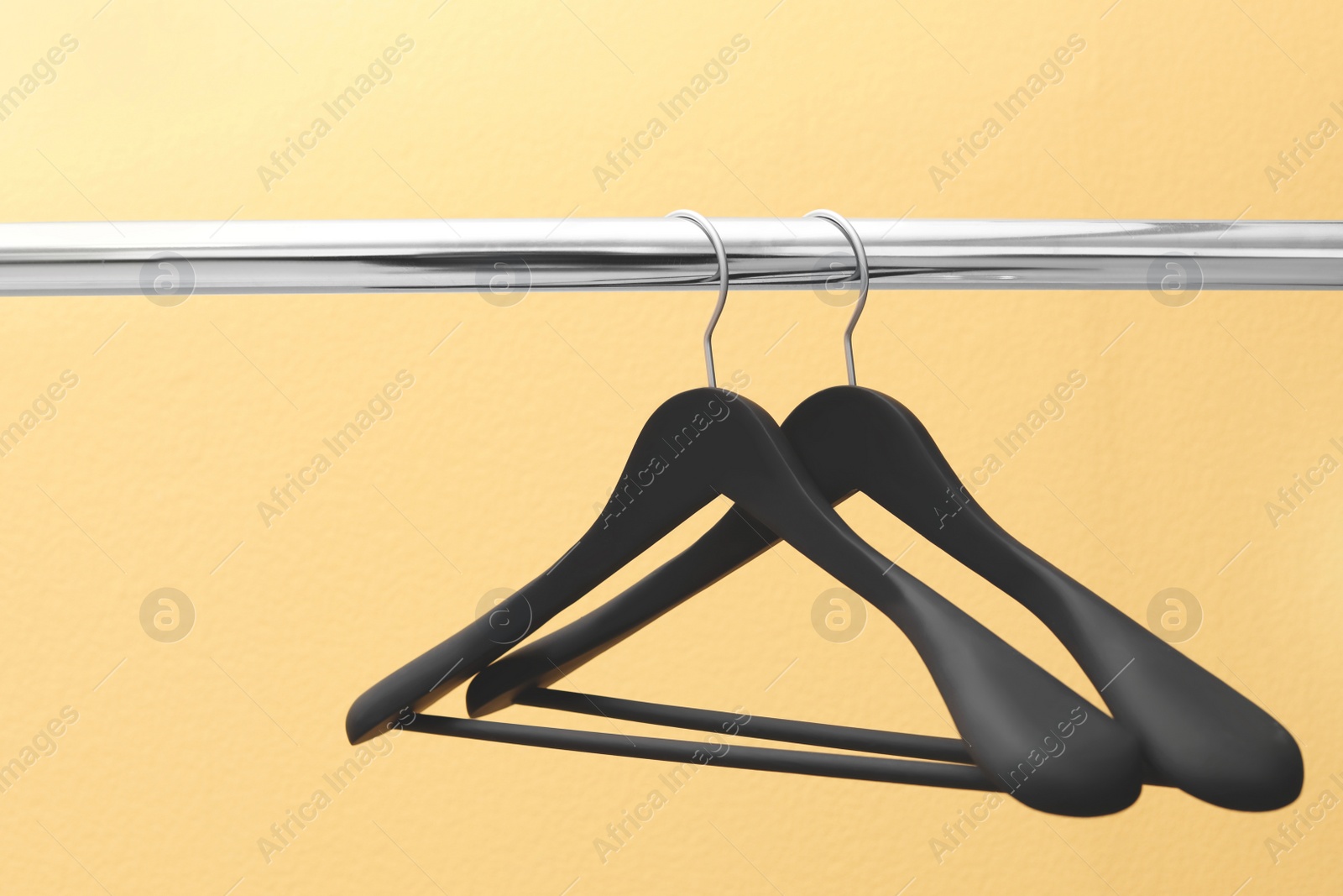 Photo of Clothes hangers on metal rail against color background