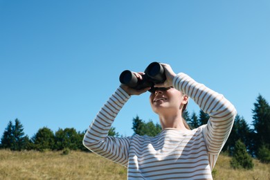 Woman looking through binoculars outdoors on sunny day