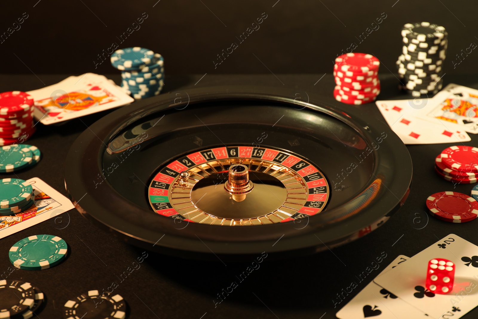 Photo of Roulette wheel, playing cards and chips on table, closeup. Casino game