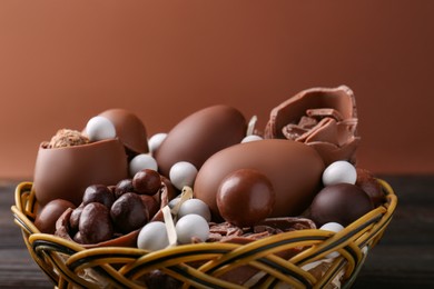 Photo of Tasty chocolate eggs and sweets in wicker basket on brown background