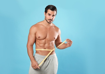 Photo of Young man with slim body using measuring tape on light blue background