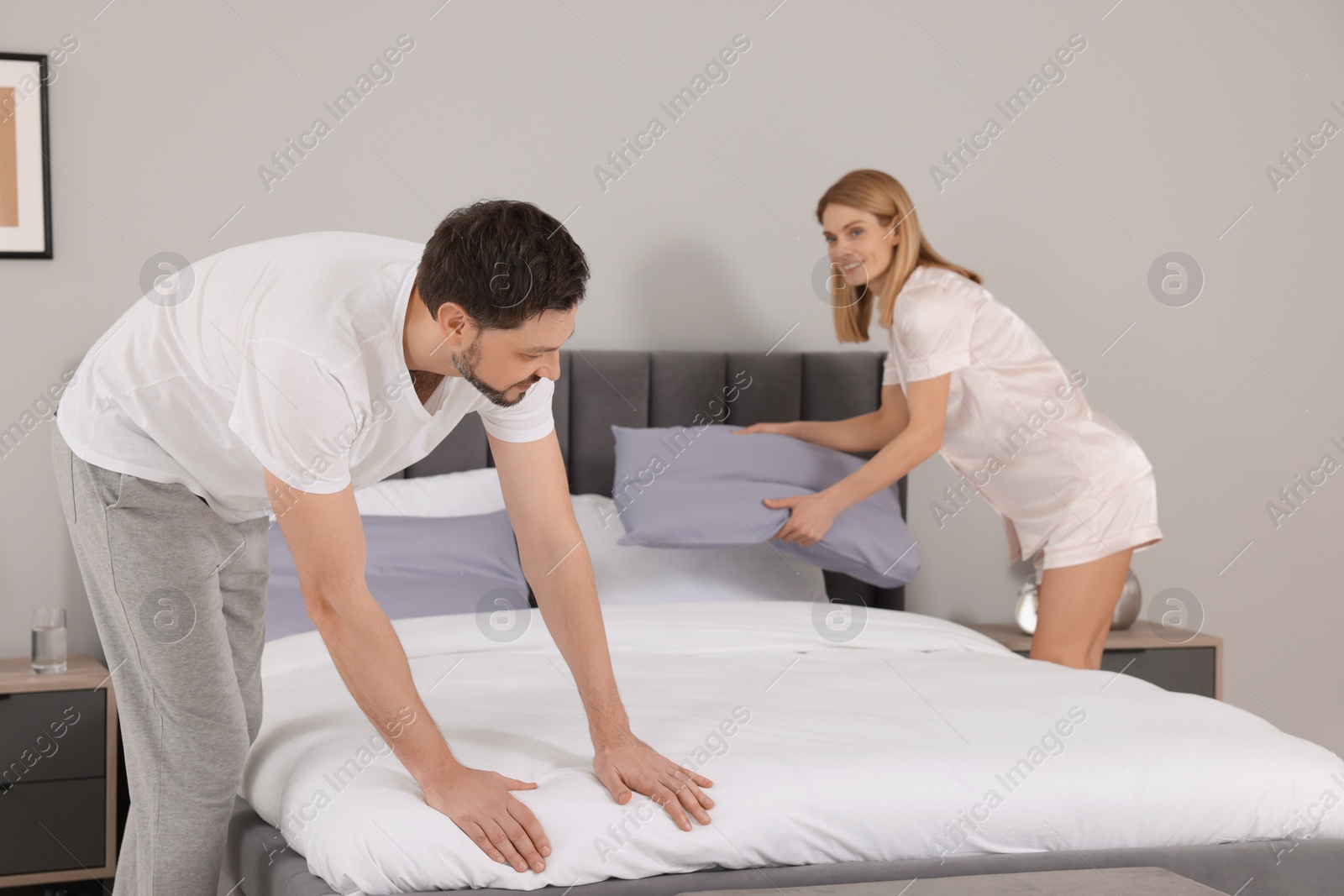 Photo of Couple changing bed linens in room. Domestic chores