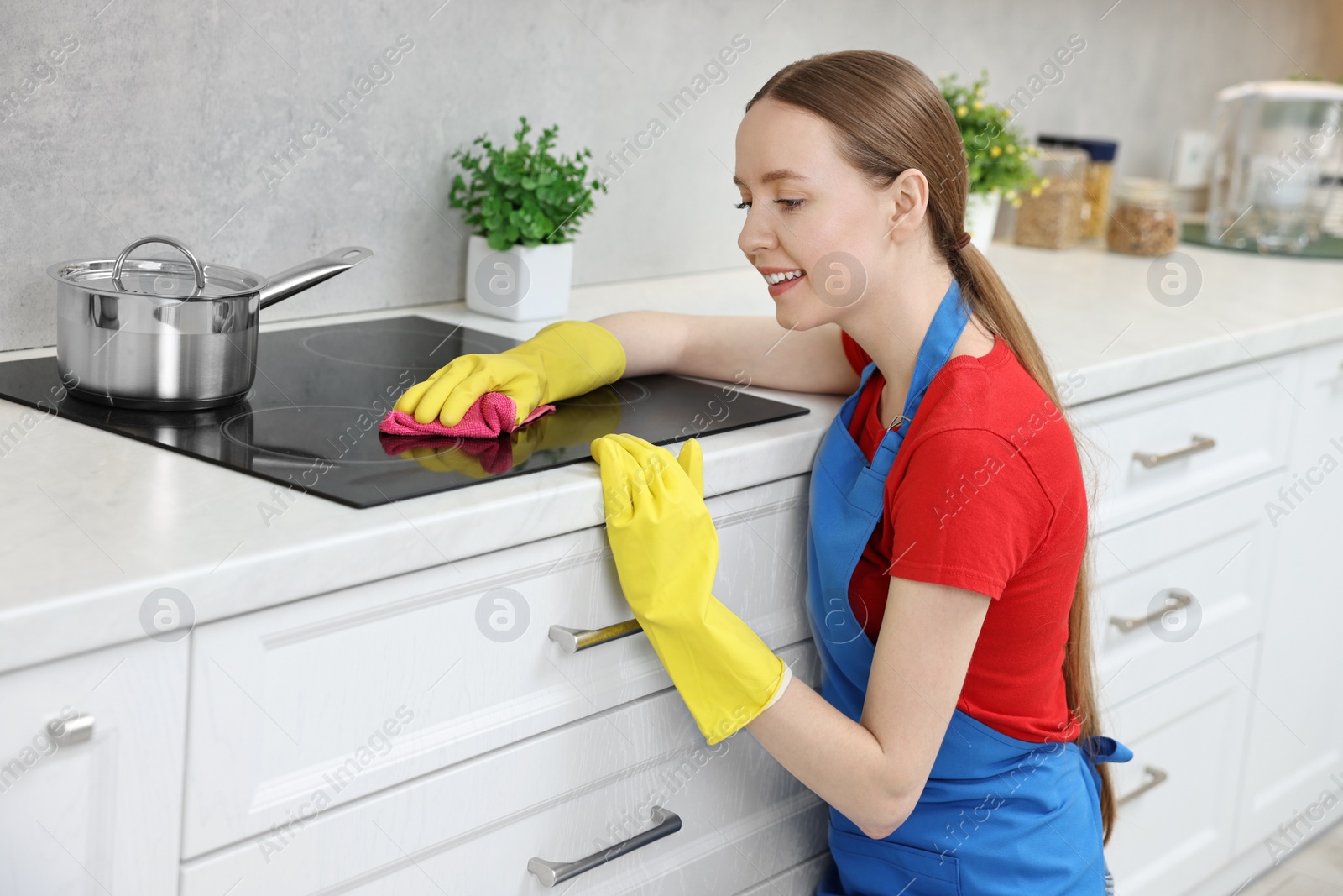 Photo of Woman cleaning electric stove with rag in kitchen