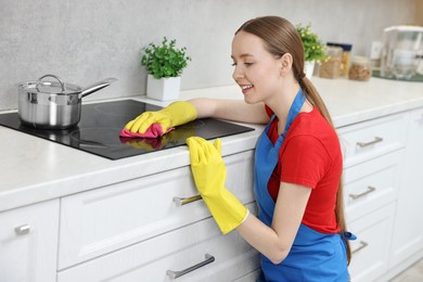 Photo of Woman cleaning electric stove with rag in kitchen