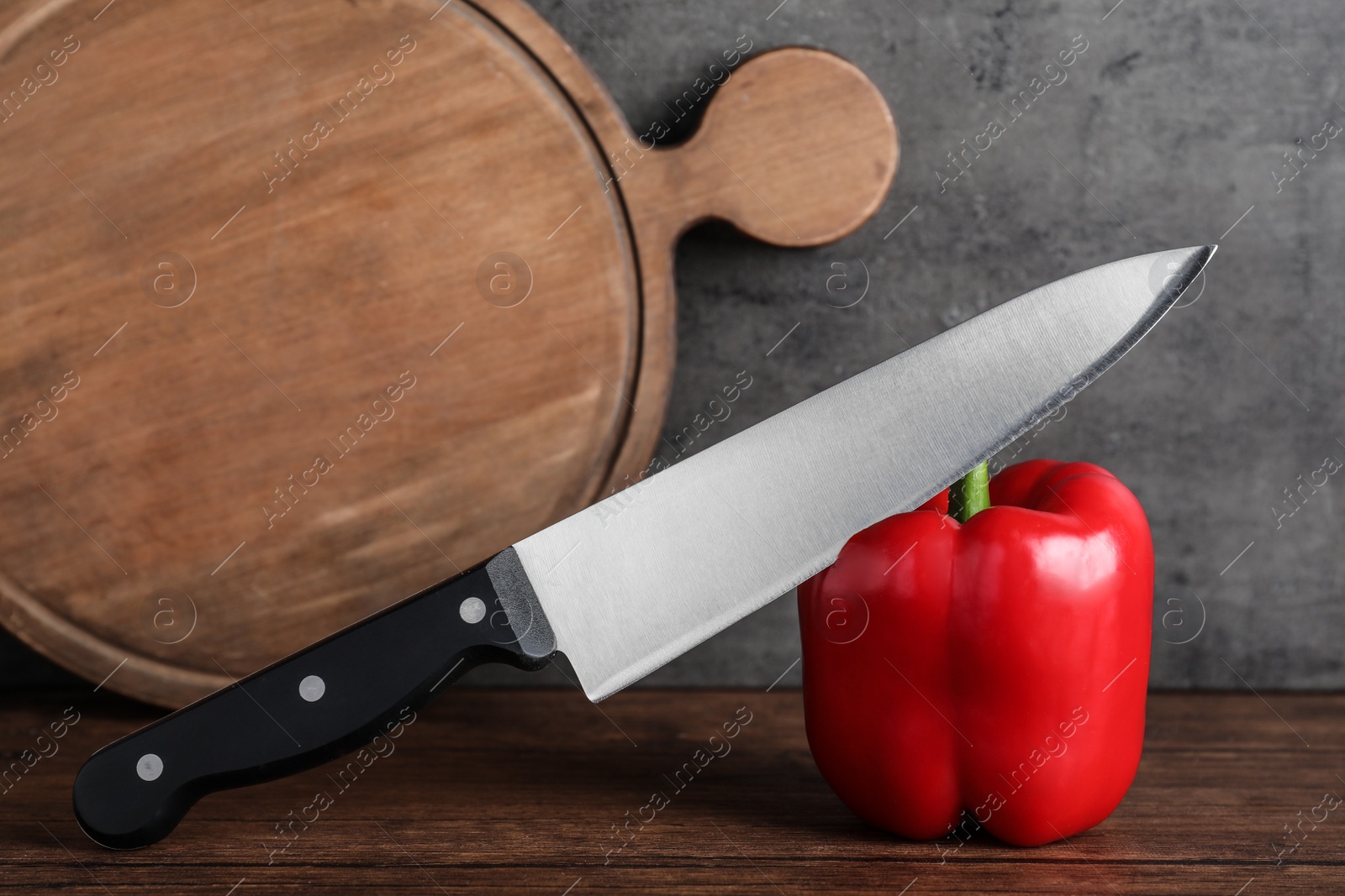 Photo of Chef knife, bell pepper and serving board on wooden table against grey background. Clean dishes