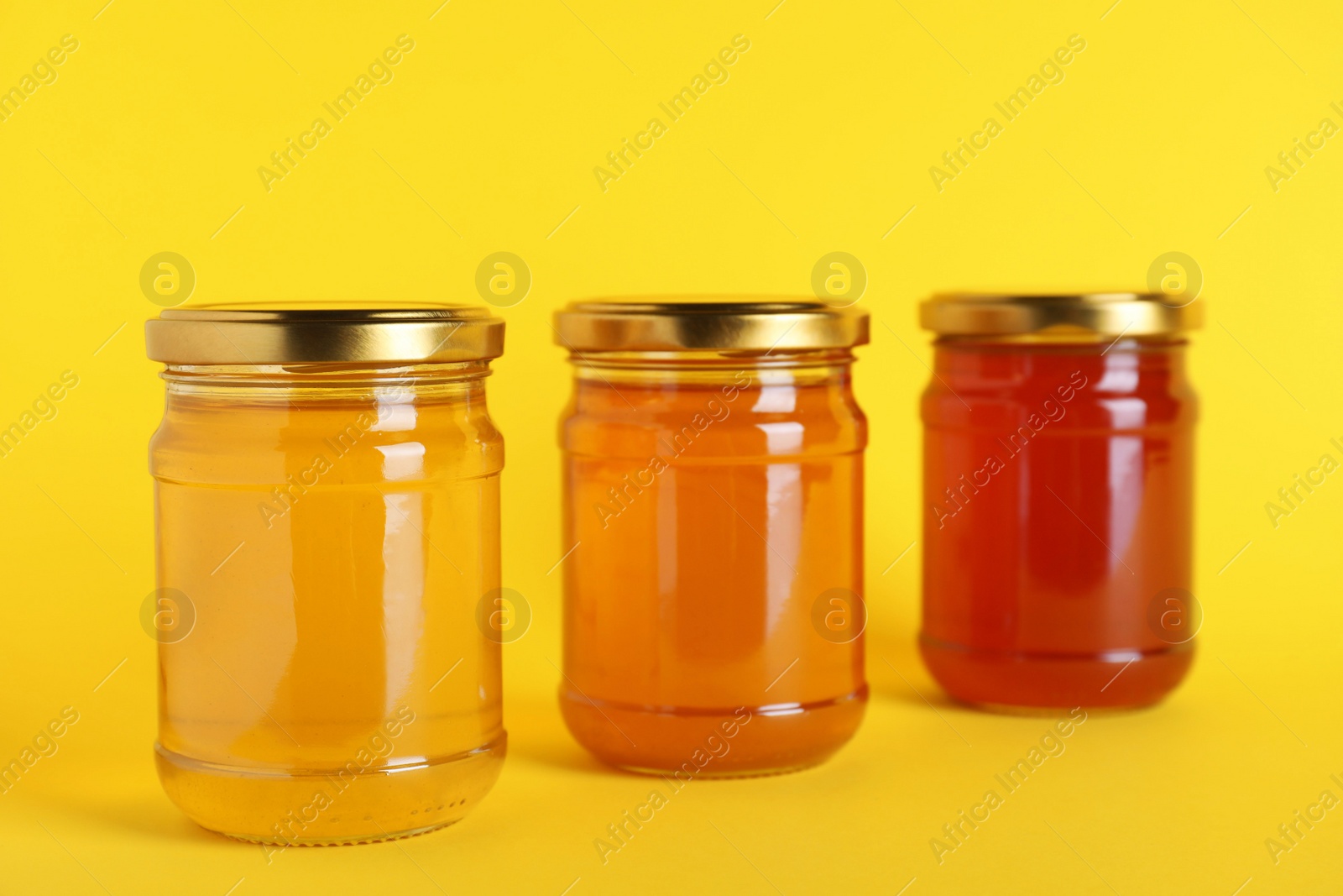 Photo of Jars with different types of organic honey on yellow background