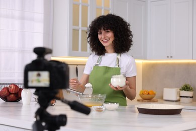 Photo of Smiling food blogger cooking while recording video in kitchen