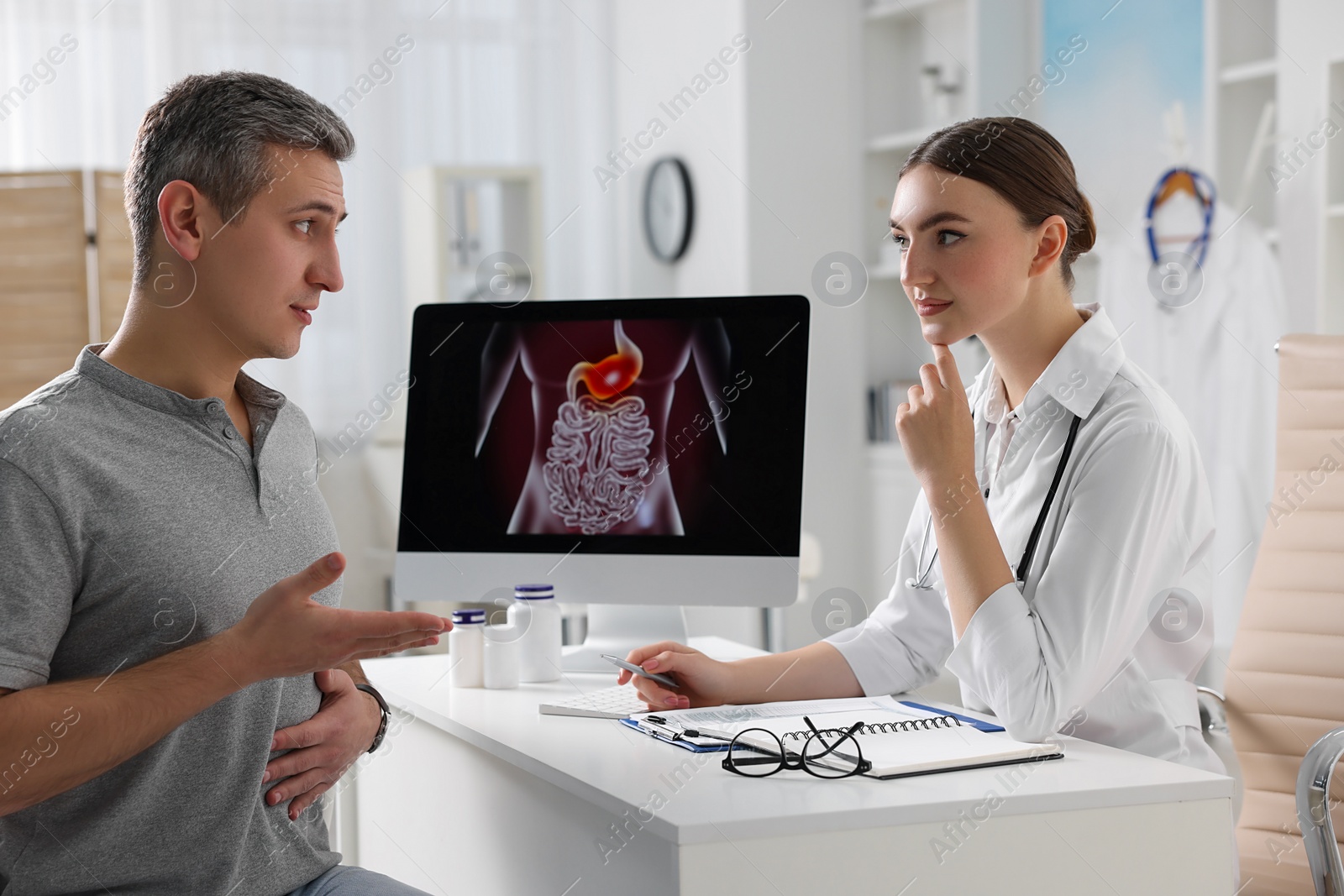 Photo of Gastroenterologist consulting patient with stomach pain at table in clinic