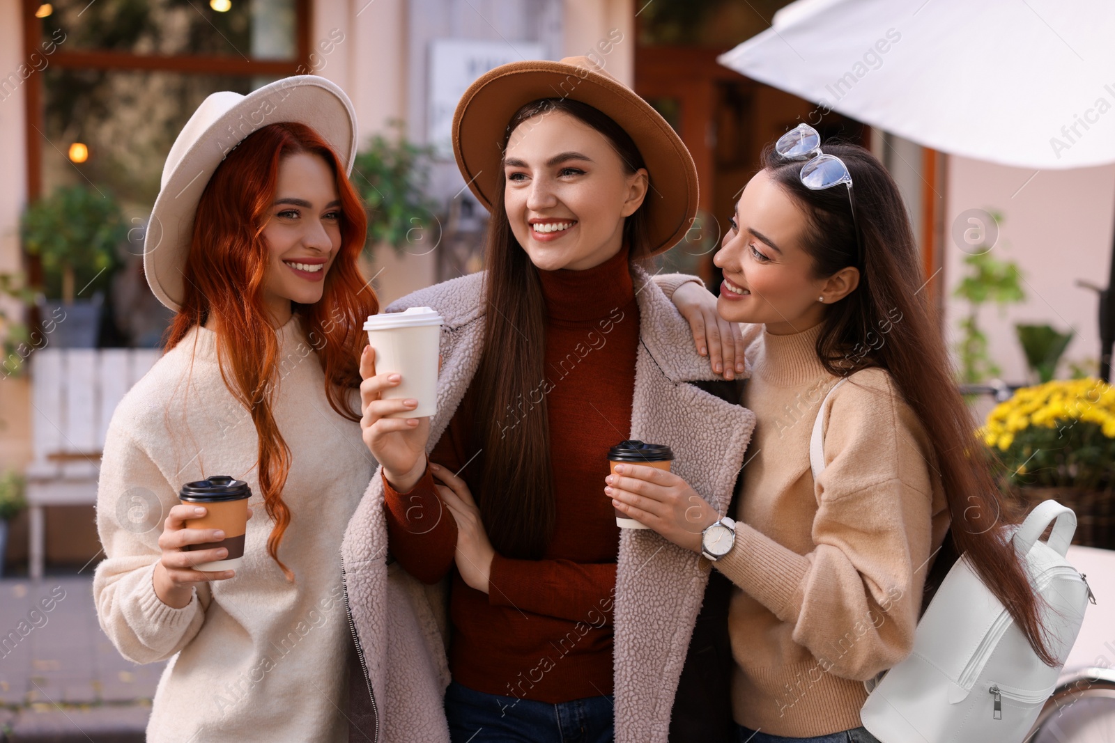 Photo of Happy friends with paper cups of coffee spending time together on city street