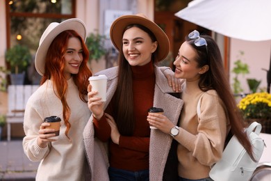 Photo of Happy friends with paper cups of coffee spending time together on city street