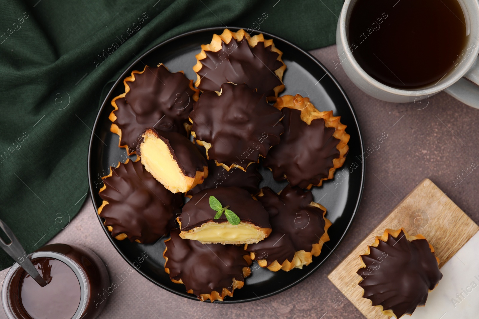 Photo of Delicious profiteroles with chocolate spread, cream and aromatic tea on textured table, flat lay