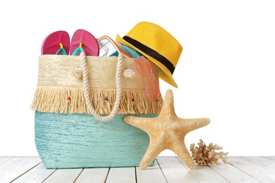 Stylish bag with beach accessories on wooden table against white background