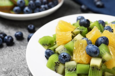 Plate of tasty fruit salad on grey textured table, closeup