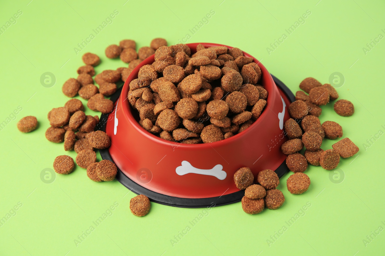 Photo of Dry dog food and feeding bowl on light green background