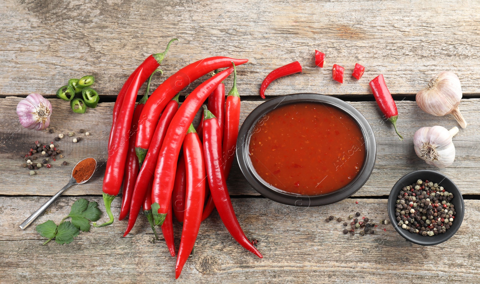 Photo of Spicy chili sauce in bowl and ingredients on wooden table, flat lay