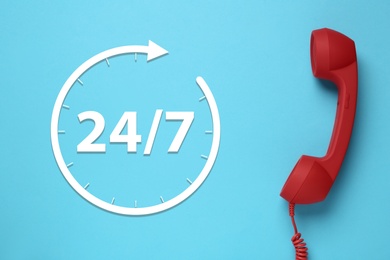 Image of 24/7 hotline service. Red handset on light blue background, top view